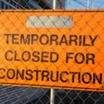 Orange sign behind fence reading 'Temporarily Closed for Construction' at site.